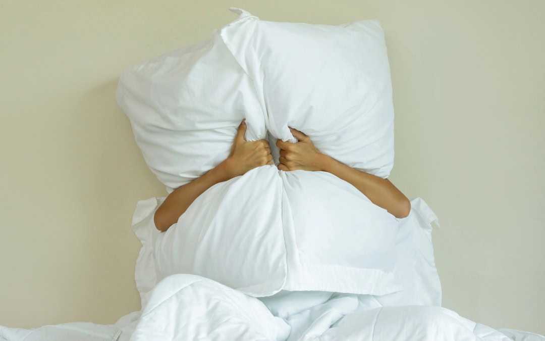 Good Neighbours - photo of person in bed holding pillows over head to block noise