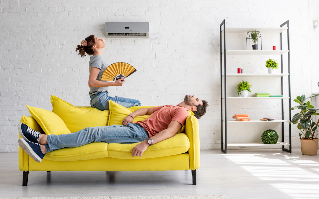 Hot Issue Requires Cool Heads - young couple lounging in room with AC not working woman using fan to keep cool